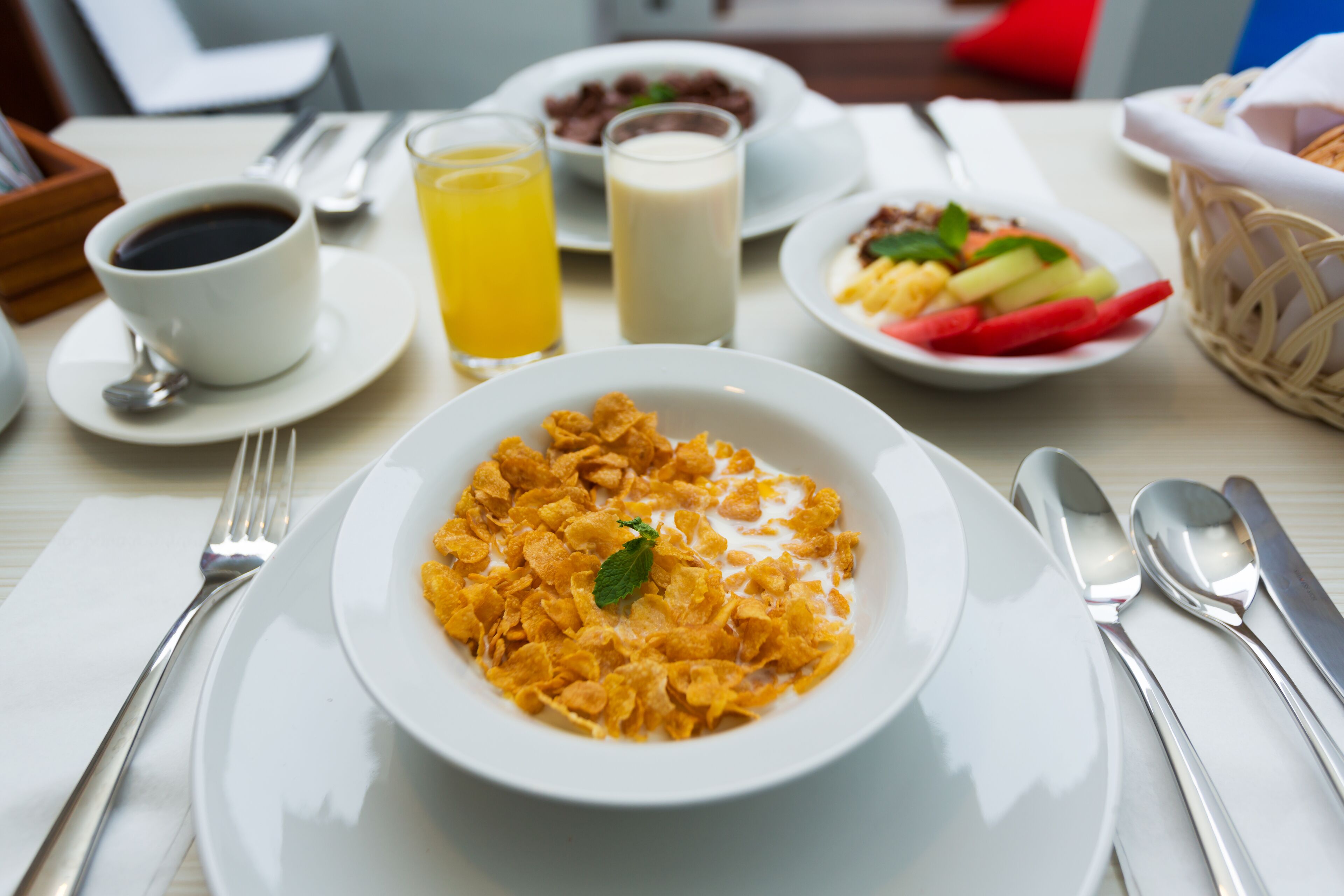 A breakfast setting with cereal, milk, orange juice, and a coffee cup on a table.