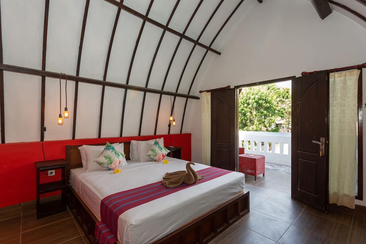 Un dormitorio con cama, mesitas de noche, un banco y vistas al exterior.