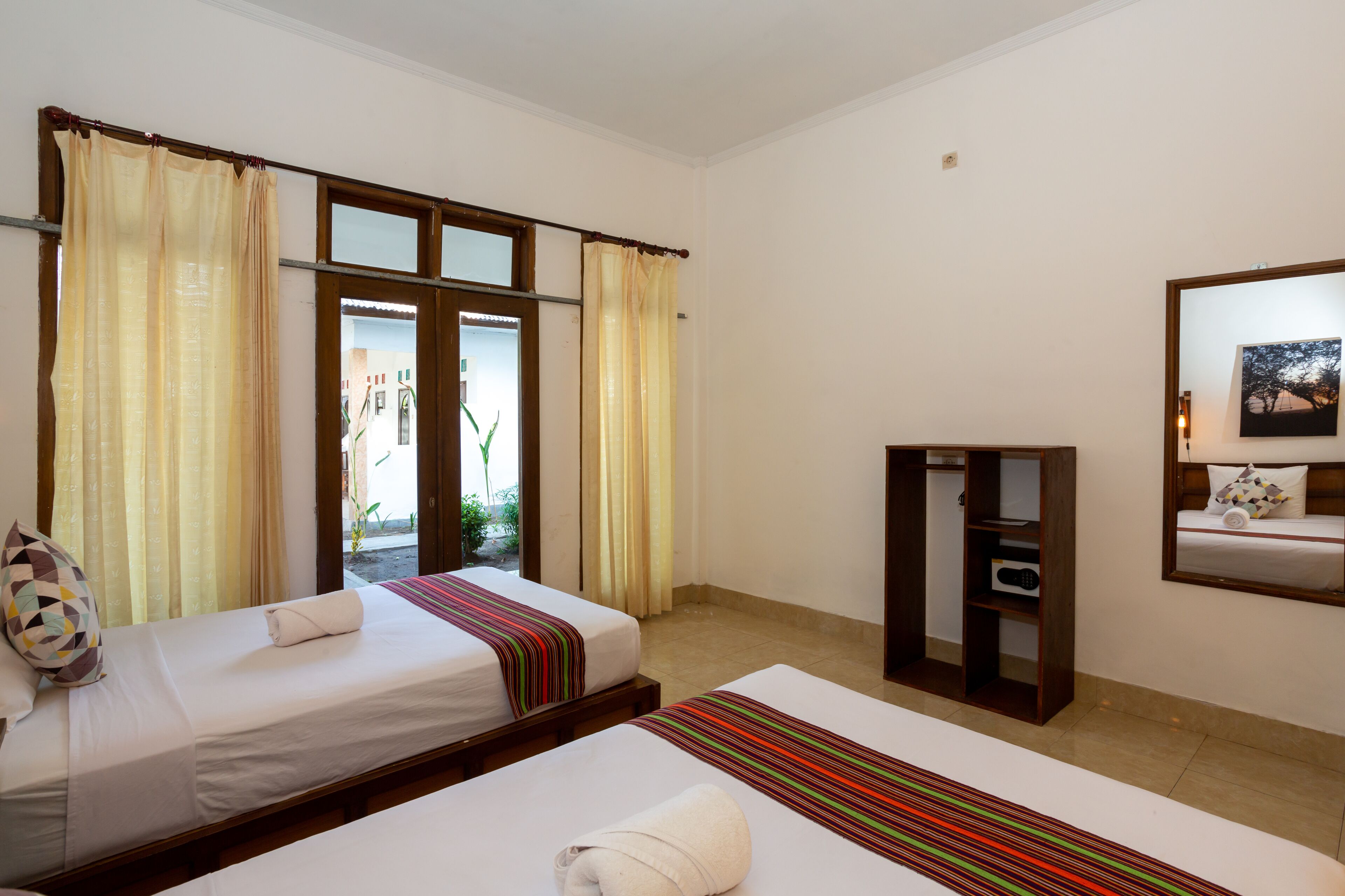 A hotel room with two beds, a wooden wardrobe, a mirror, and a window with curtains.