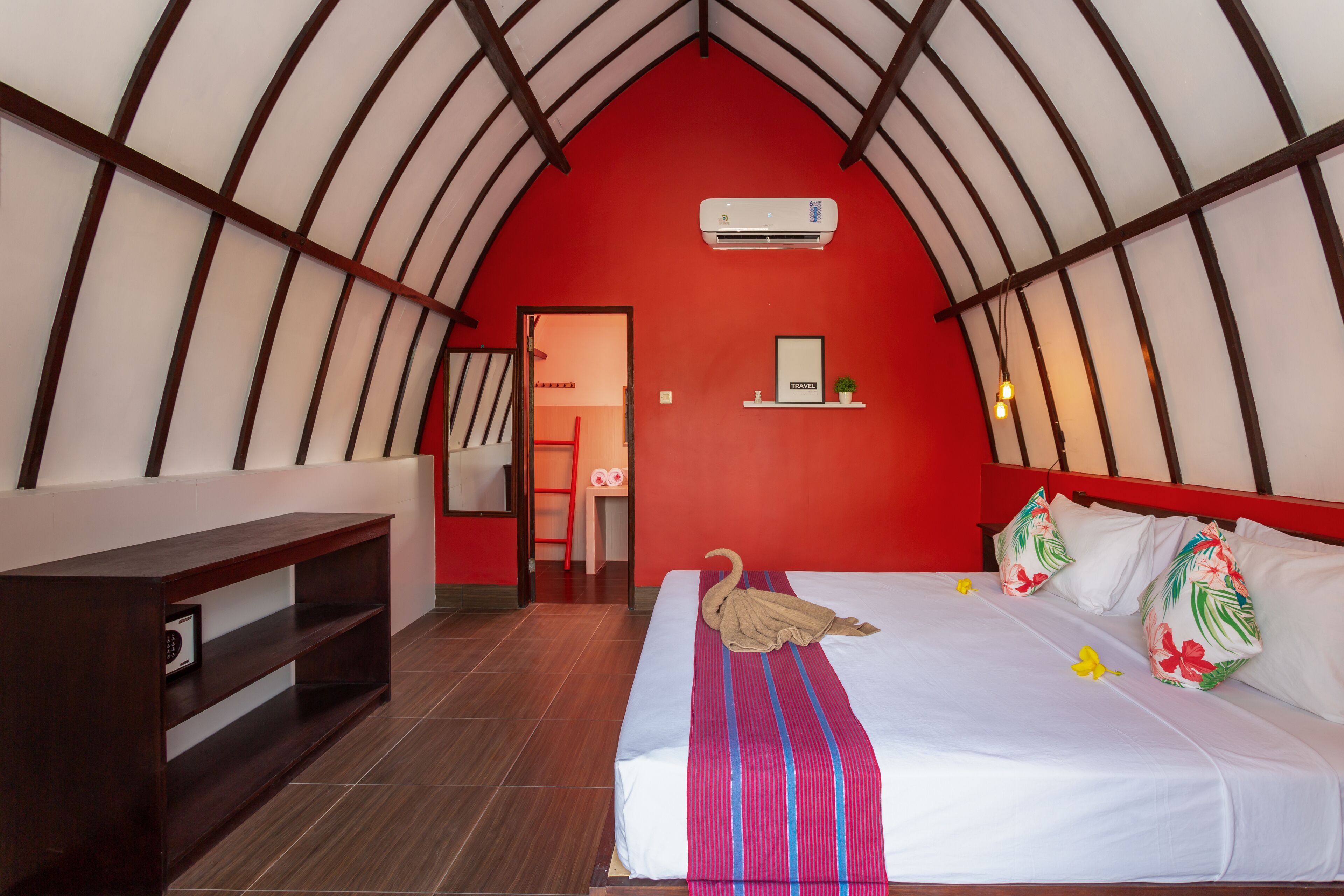 A hotel room with a red ceiling, a bed with a swan-shaped towel, and a shelf with a plant and a sign.