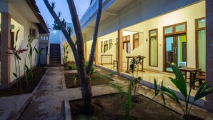 Un patio con zona de estar cubierta, palmeras y una escalera que lleva a un nivel superior.