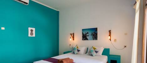 A hotel room with a bed, teal walls, a painting, and a wall-mounted air conditioner.