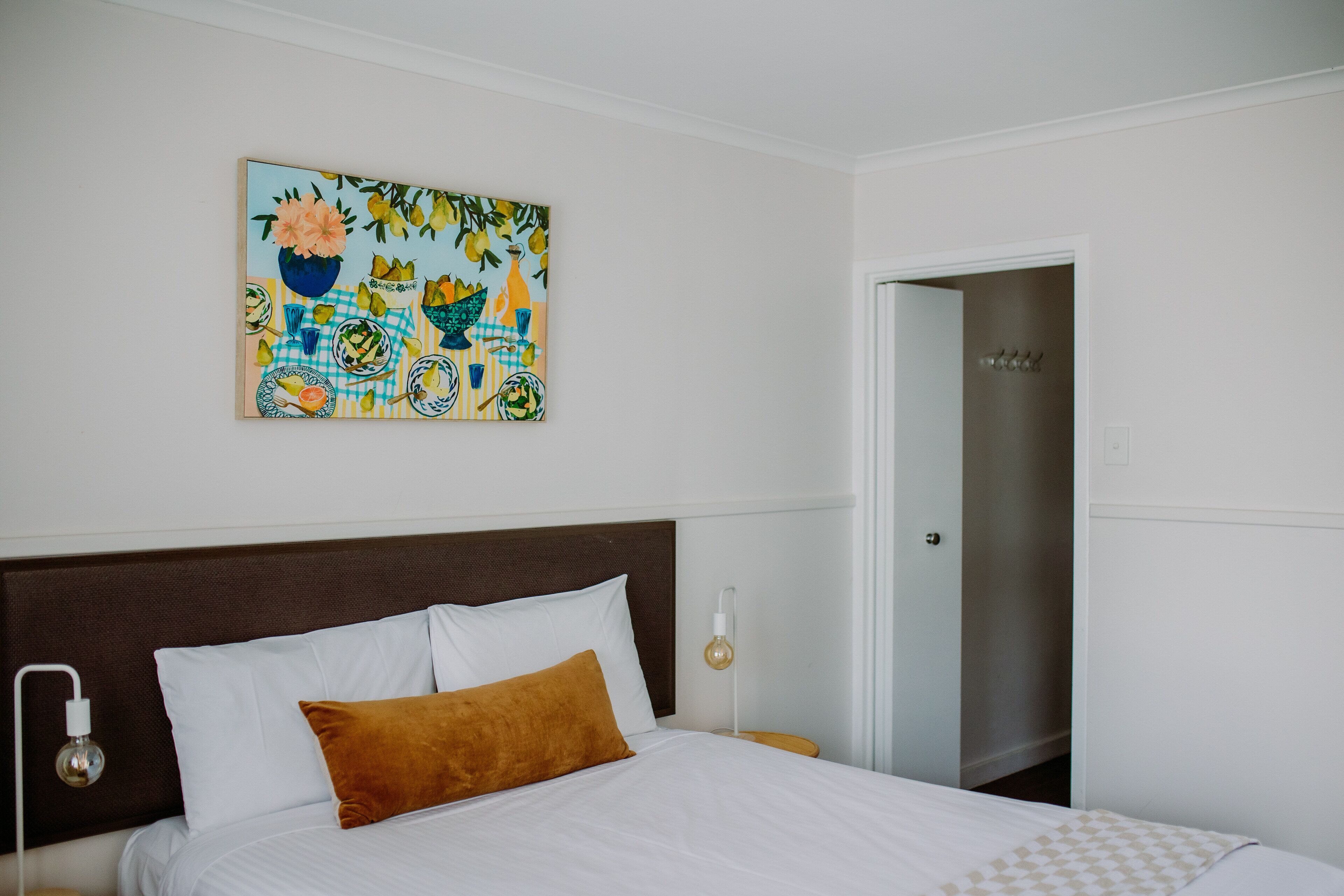 Habitación de hotel con una cama, una mesita de noche, una lámpara de pared y una puerta.