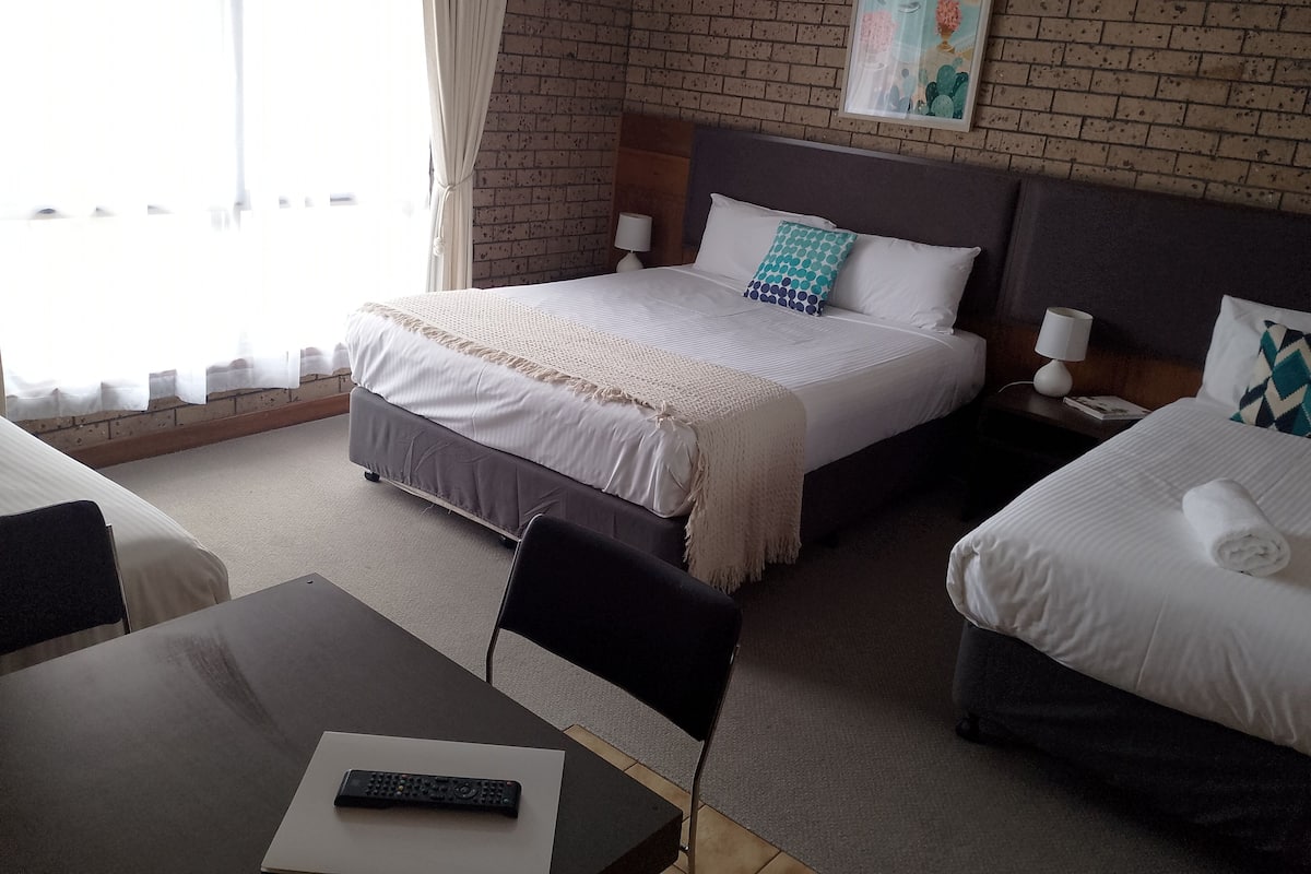 A hotel room with a large bed, a smaller bed, a desk with a remote control, and a painting on the wall.