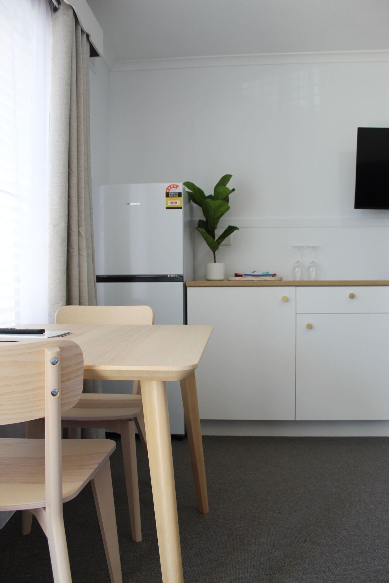 A compact kitchen with a white refrigerator, a small potted plant, and a wooden table with chairs.