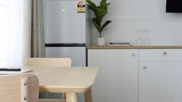 Une cuisine de taille modeste, avec un réfrigérateur blanc, une petite plante en pot et une table en bois avec des chaises.