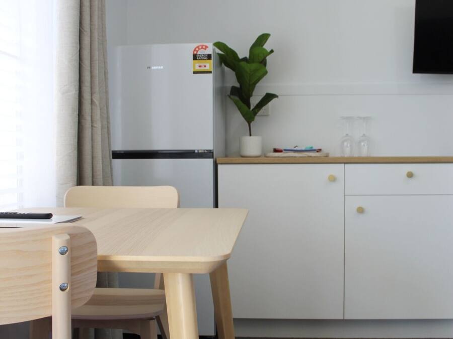 Une cuisine de taille modeste, avec un réfrigérateur blanc, une petite plante en pot et une table en bois avec des chaises.