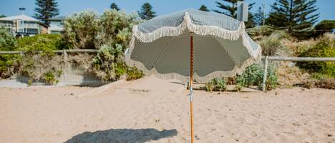 Una sombrilla con dosel a rayas, una toalla de playa y un sombrero de paja sobre la arena.