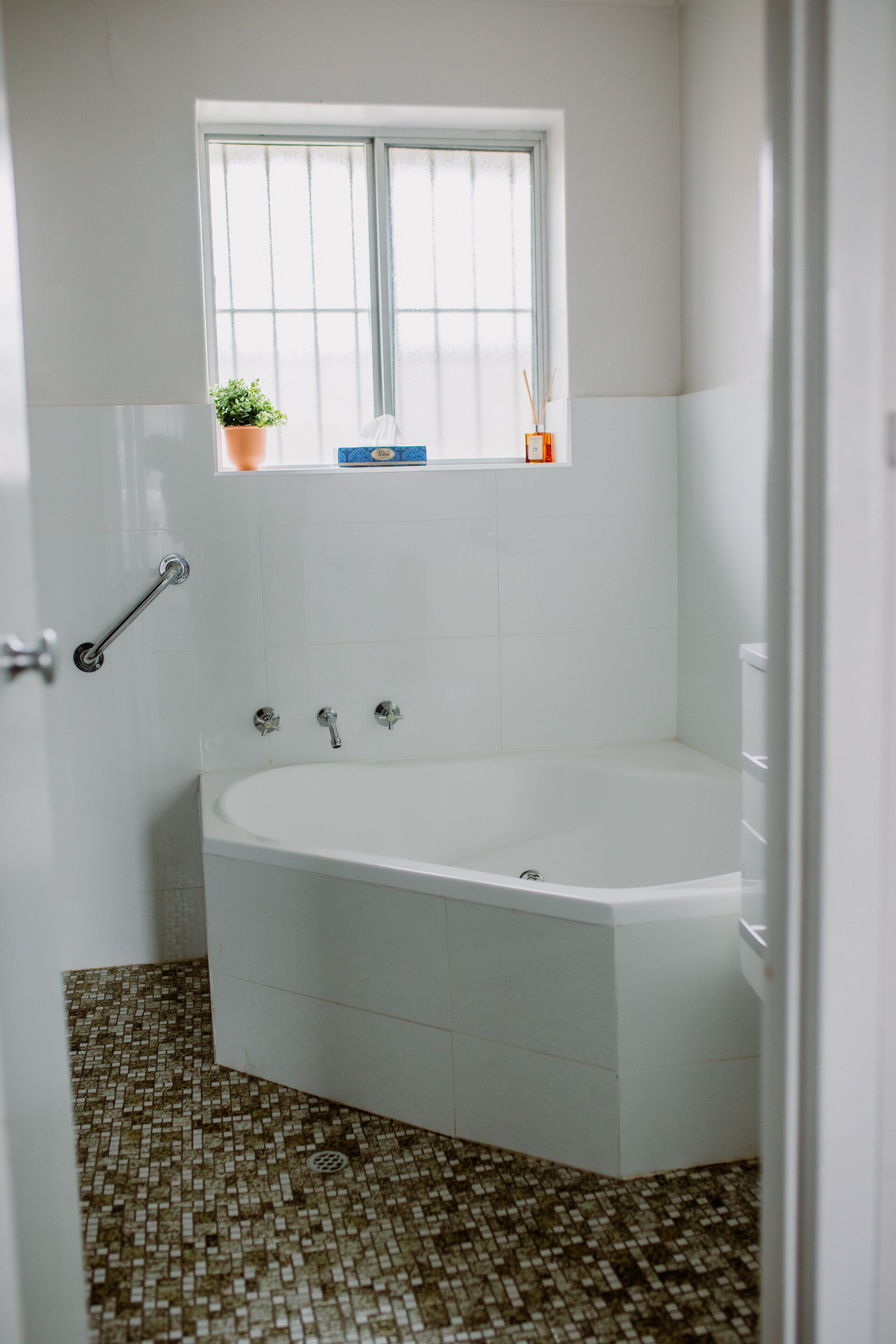 Un baño con una bañera blanca, una ventana encima y piso de baldosas.
