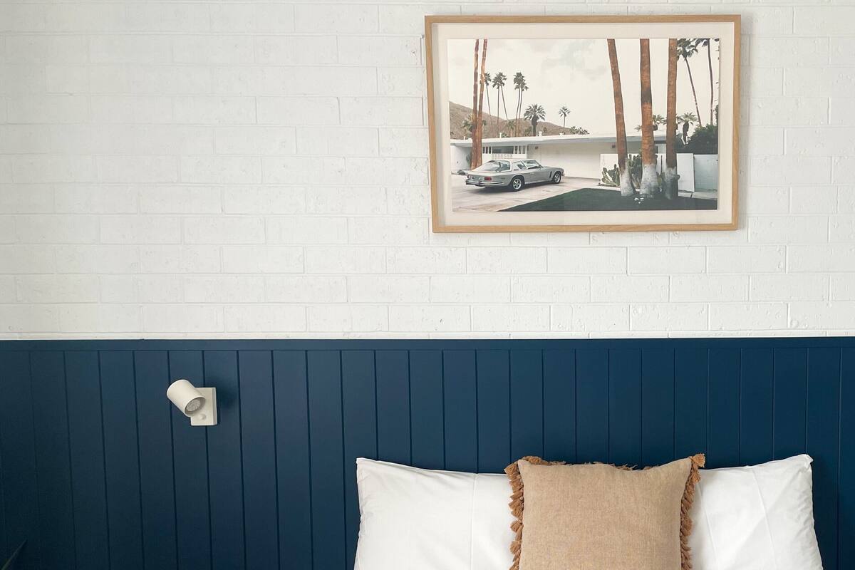 A bedroom with a white bed, a blue headboard, a small wooden side table, and a framed picture on the wall.