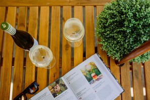 A wooden table with a bottle, two glasses of white wine, a pair of glasses, and a book with travel pages visible. - Pan Co Victor Harbor (Victor Harbor)