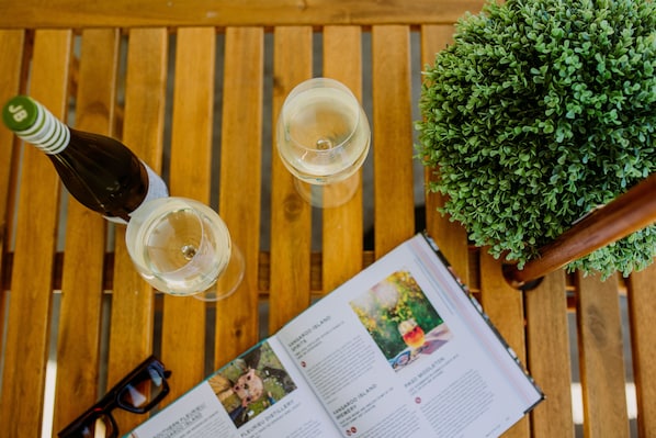 A wooden table with a bottle, two glasses of white wine, a pair of glasses, and a book with travel pages visible. - Pan Co Victor Harbor (Victor Harbor)