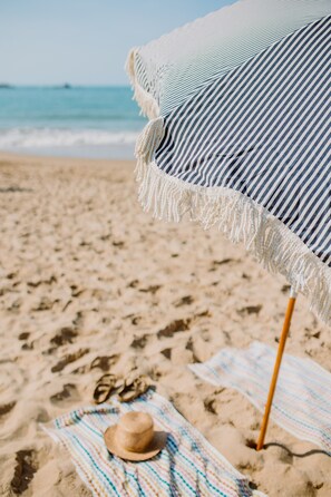 A beach scene with a striped beach umbrella, a straw hat, and flip-flops on a towel. - Pan Co Victor Harbor (Victor Harbor)