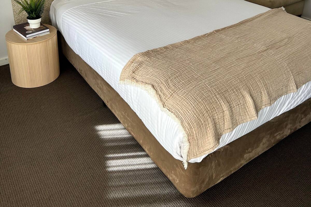 A hotel room with a large bed, a round side table, a small sofa, and a wall-mounted lamp.