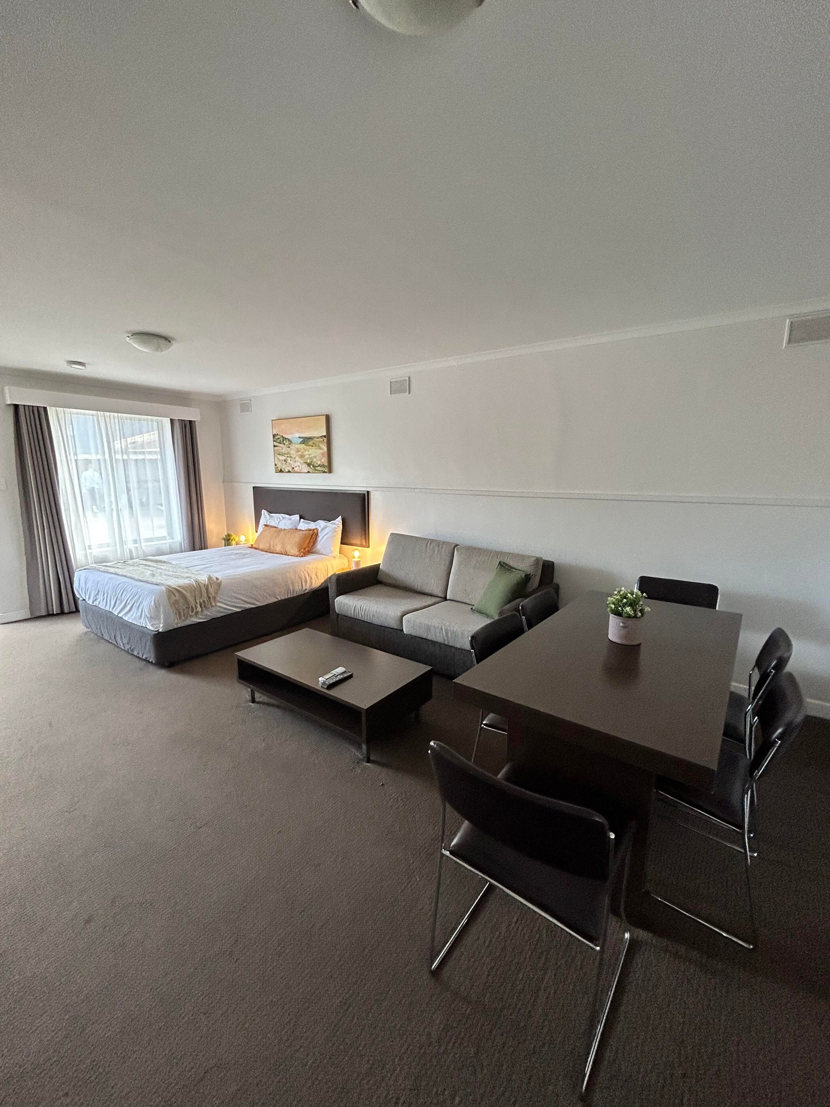 A modern hotel room with a bed, sofa, dining table, and chairs.