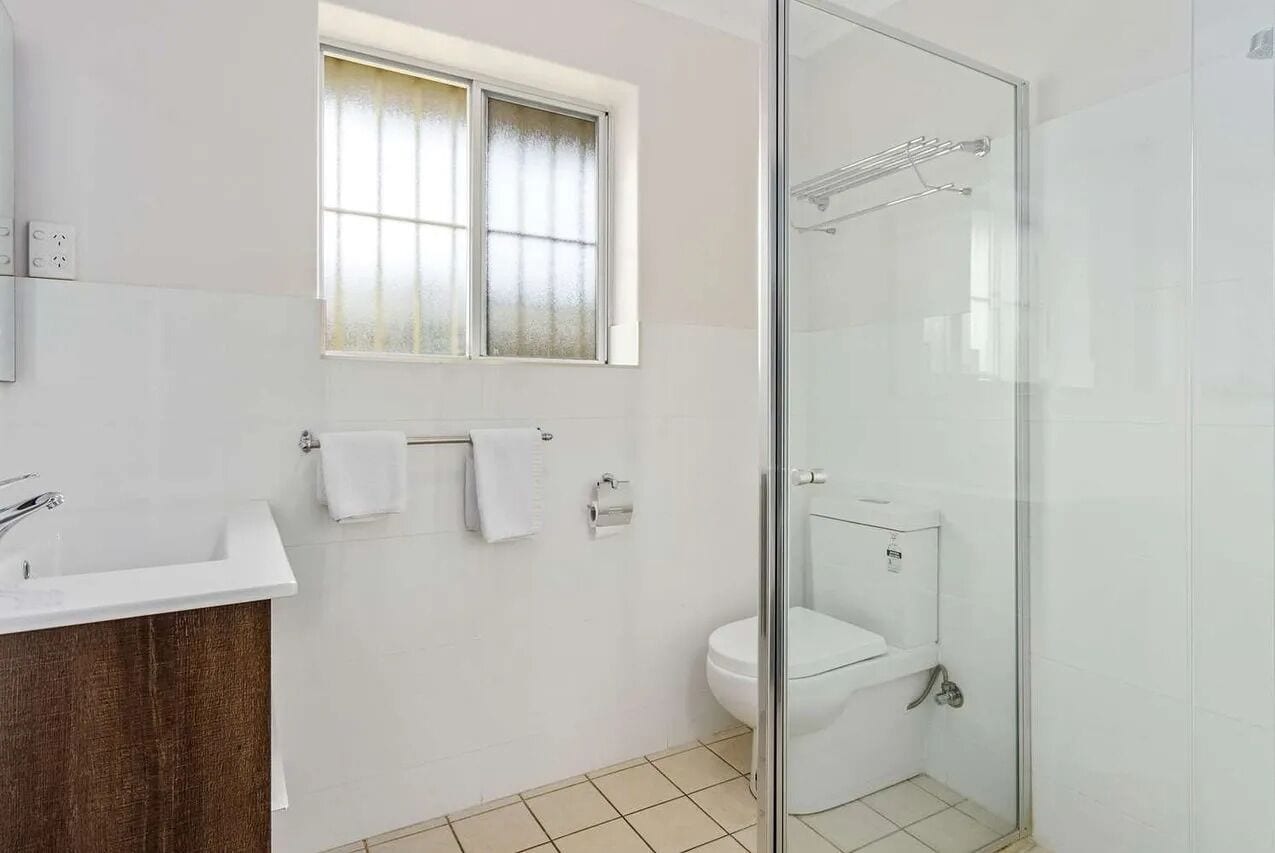 Une salle de bain moderne avec une douche à parois de verre, un lavabo blanc et une fenêtre en verre dépoli.