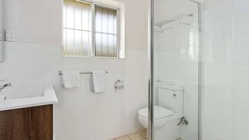 Un baño moderno con ducha envuelta en cristal, un lavabo blanco y una ventana con vidrio esmerilado.