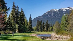A golf course with a pond, surrounded by tall trees and mountains in the background. - Green Lake condo w/ panoramic views (Whistler)