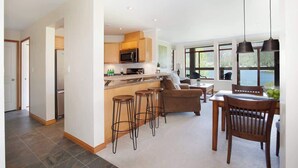 A modern kitchen with a central island, bar stools, a dining table with chairs, and large windows offering a view of the outdoors. - Green Lake condo w/ panoramic views (Whistler)
