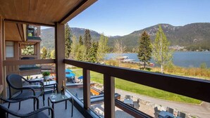 A balcony with wicker chairs and a table, overlooking a lake and mountains. - Green Lake condo w/ panoramic views (Whistler)