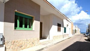 A row of buildings with a stone base and a flat roof, a paved street, and parked cars. - Luce Holiday Home With air Conditioning for 5 Guests (Melendugno)