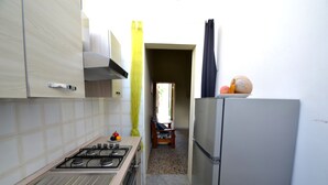 A kitchen with a gas stove, a refrigerator, and a sink. There is a chair in the background and a door leading to another room. - Luce Holiday Home With air Conditioning for 5 Guests (Melendugno)