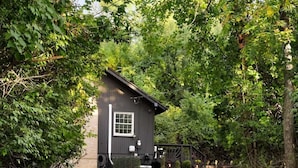 A gravel driveway leading to a small, dark-colored building surrounded by dense greenery. - Far View Shenandoah | Hot Tub, Movie & Game Room, Valley Views | 3BR & Sleeps 6 (Front Royal)