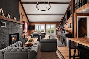 A modern living room with a fireplace, sofas, a dining area, and a kitchen with wooden accents. - Far View Shenandoah | Hot Tub, Movie & Game Room, Valley Views | 3BR & Sleeps 6 (Front Royal)