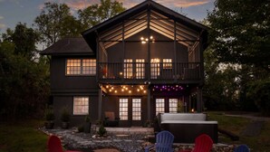 Una casa de dos pisos con balcón, zona de estar al aire libre y luces colgantes.