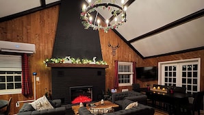 A cozy living room with a fireplace, wooden walls, and a chandelier. - Far View Shenandoah | Hot Tub, Movie & Game Room, Valley Views | 3BR & Sleeps 6 (Front Royal)