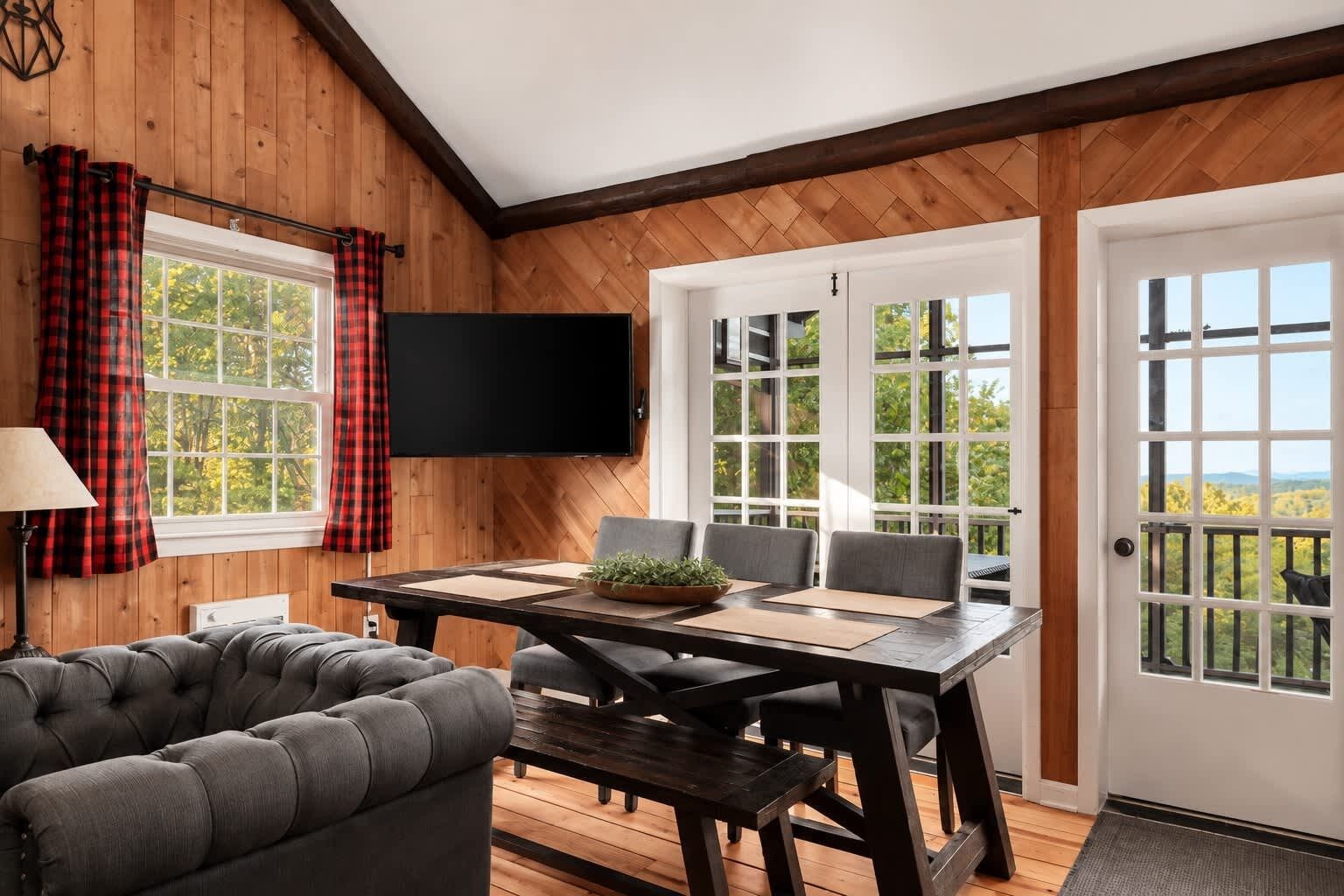 Une pièce avec un intérieur en bois, un téléviseur à écran plat fixé au mur, une table à manger avec des chaises et un canapé.