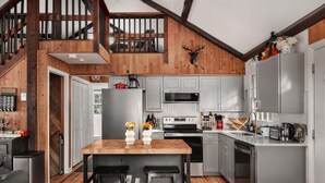 Una cocina con una mesa de madera, dos taburetes de bar, un refrigerador, un microondas, una estufa y un lavaplatos.