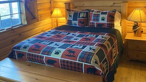 Quarto de cabana de tronco aconchegante, com uma cama, mesinhas de cabeceira de madeira, um ventilador de teto e uma janela.