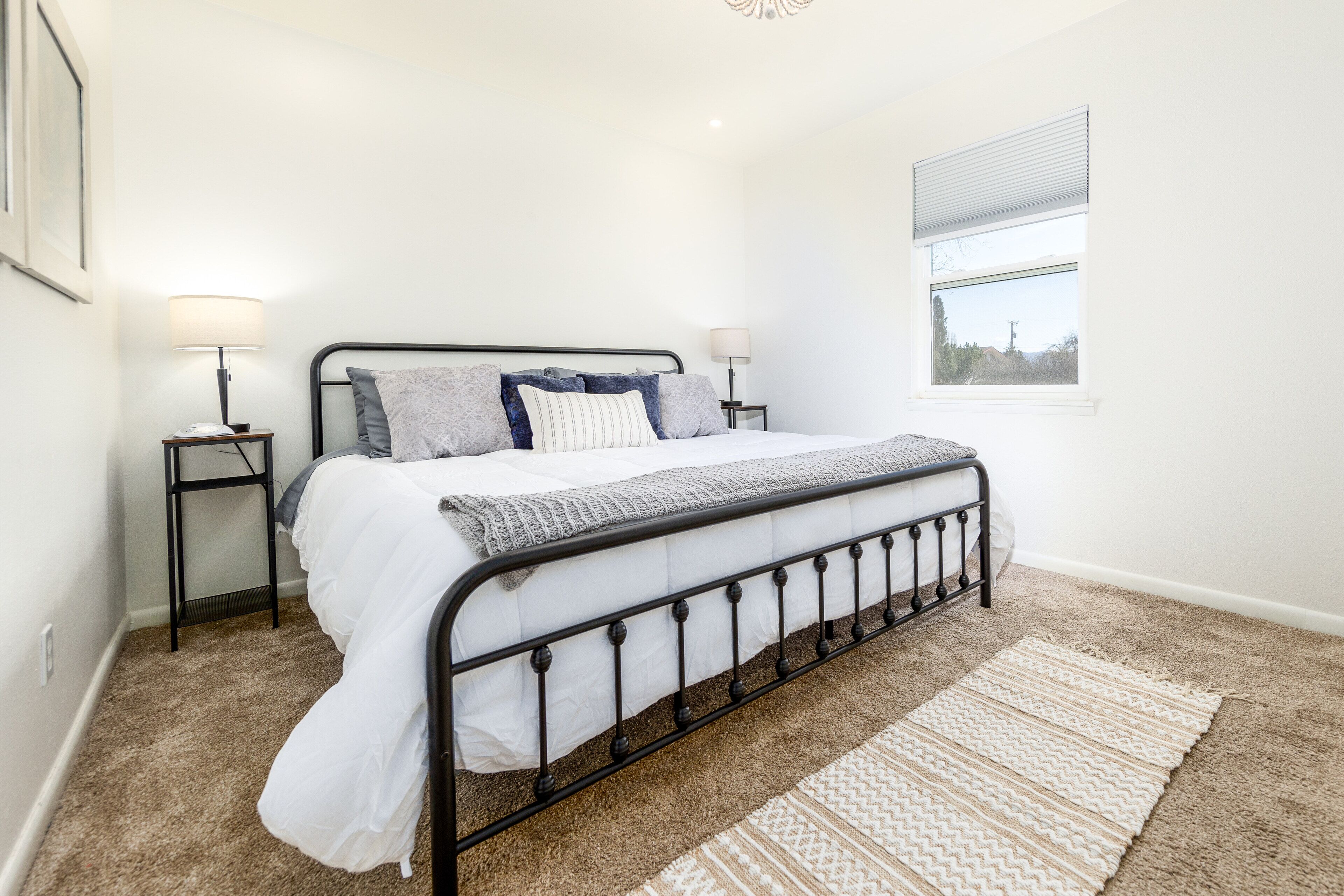 Une chambre à coucher avec un lit, deux tables de chevet, une fenêtre et un tapis.