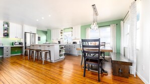 Une cuisine spacieuse avec un plancher en bois, des armoires blanches et un îlot central doté de tabourets.