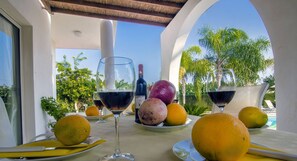 A table with wine glasses, lemons, and a pomegranate, set against a view of palm trees and a clear sky.