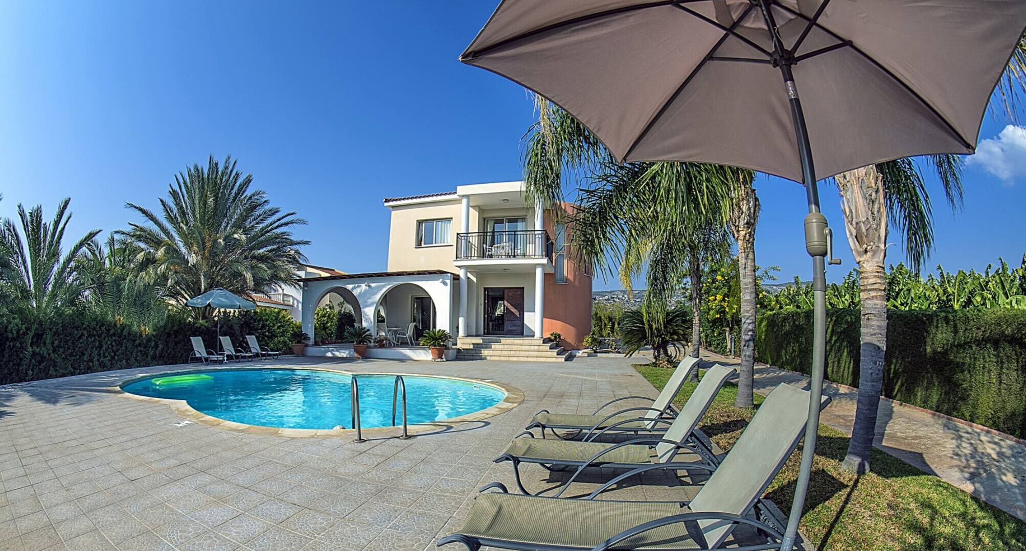 A pool with lounge chairs, a building with a balcony, and palm trees.