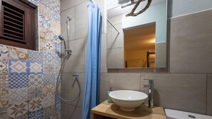 A bathroom with a tiled shower area, a sink, and a toilet.