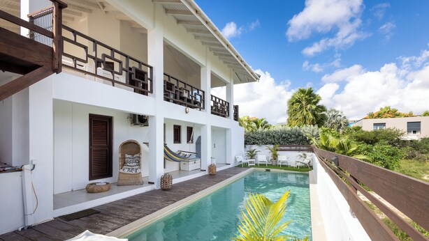A two-story building with a pool, outdoor seating, and a wooden deck.
