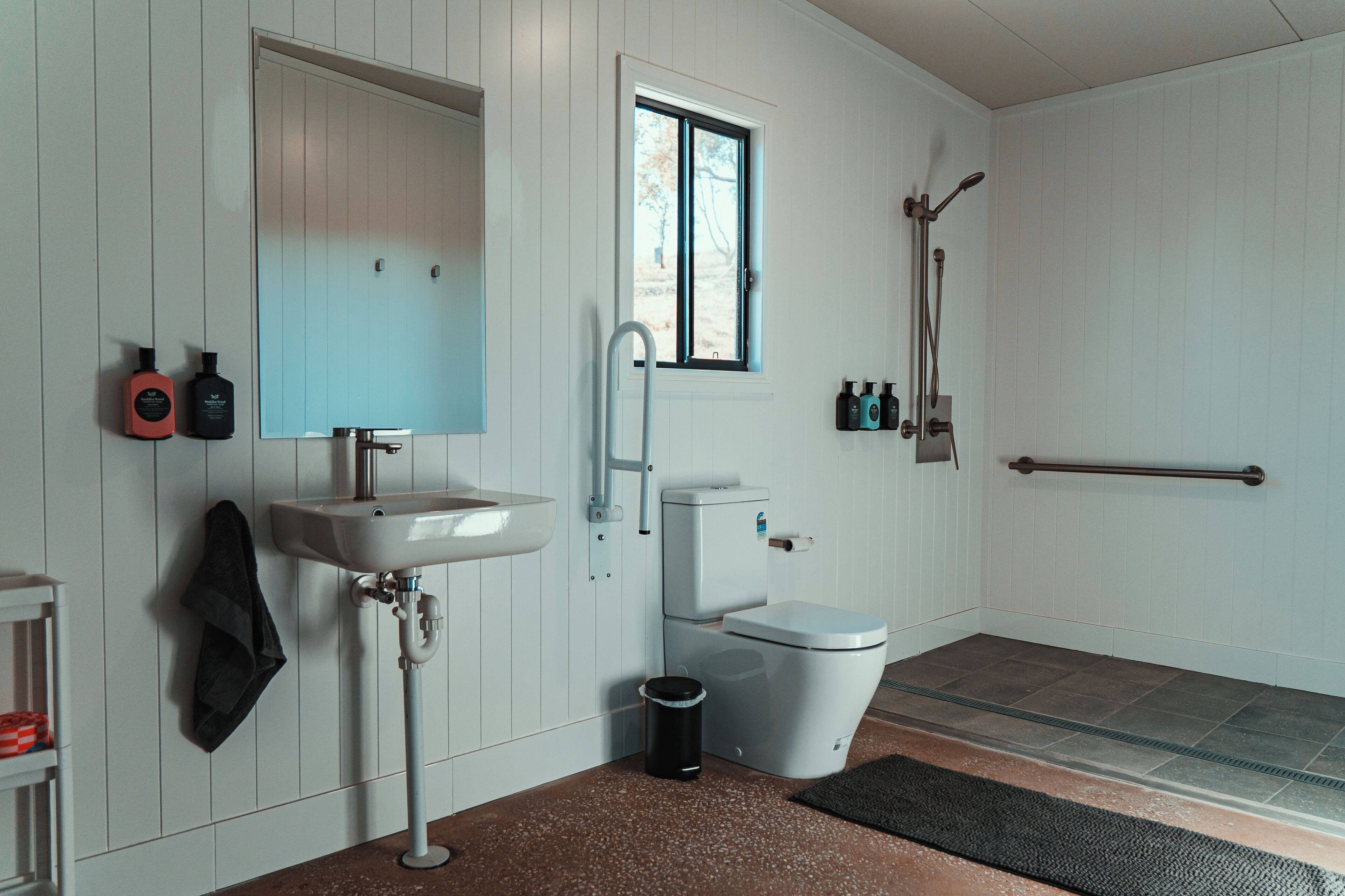 A bathroom with a white sink, a toilet, a window, and a shower area.