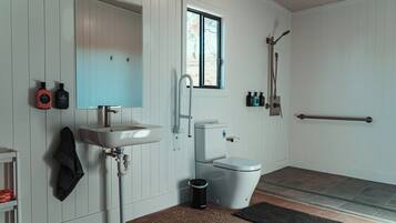 A bathroom with a white sink, a toilet, a window, and a shower area.