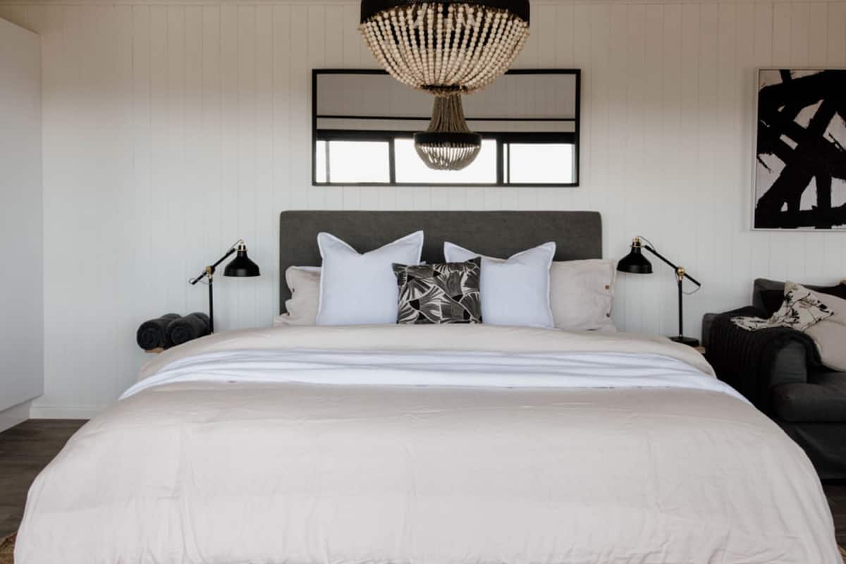 A modern bedroom with a large bed, two bedside tables, a chandelier, and a black and white abstract painting on the wall.