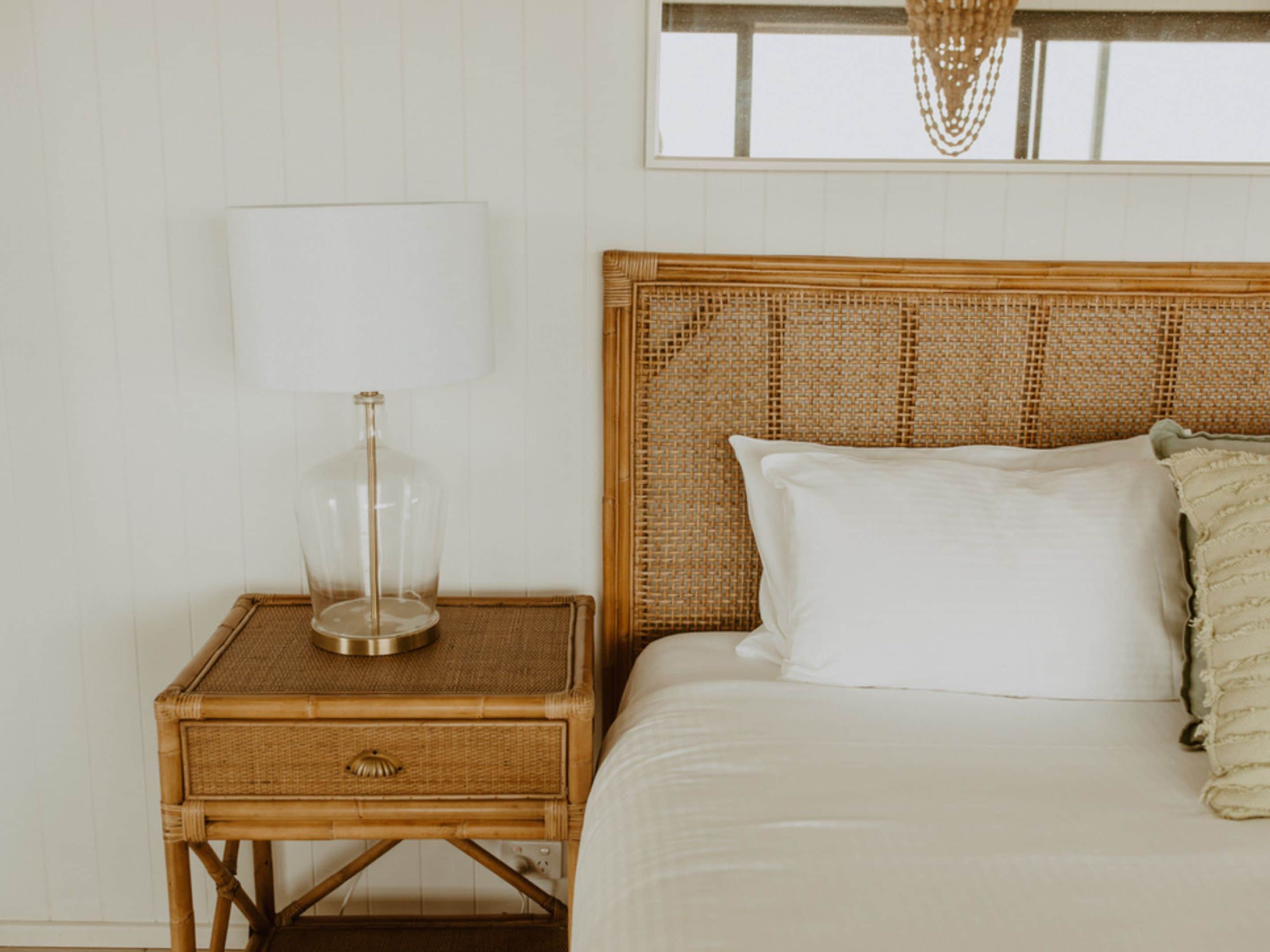 A bed with a woven headboard, a bedside table with a lamp, and a window above.