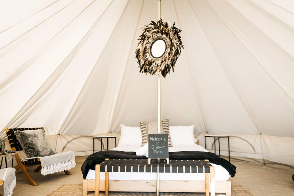 A tent with a bed, a hanging mirror, and a welcome sign.