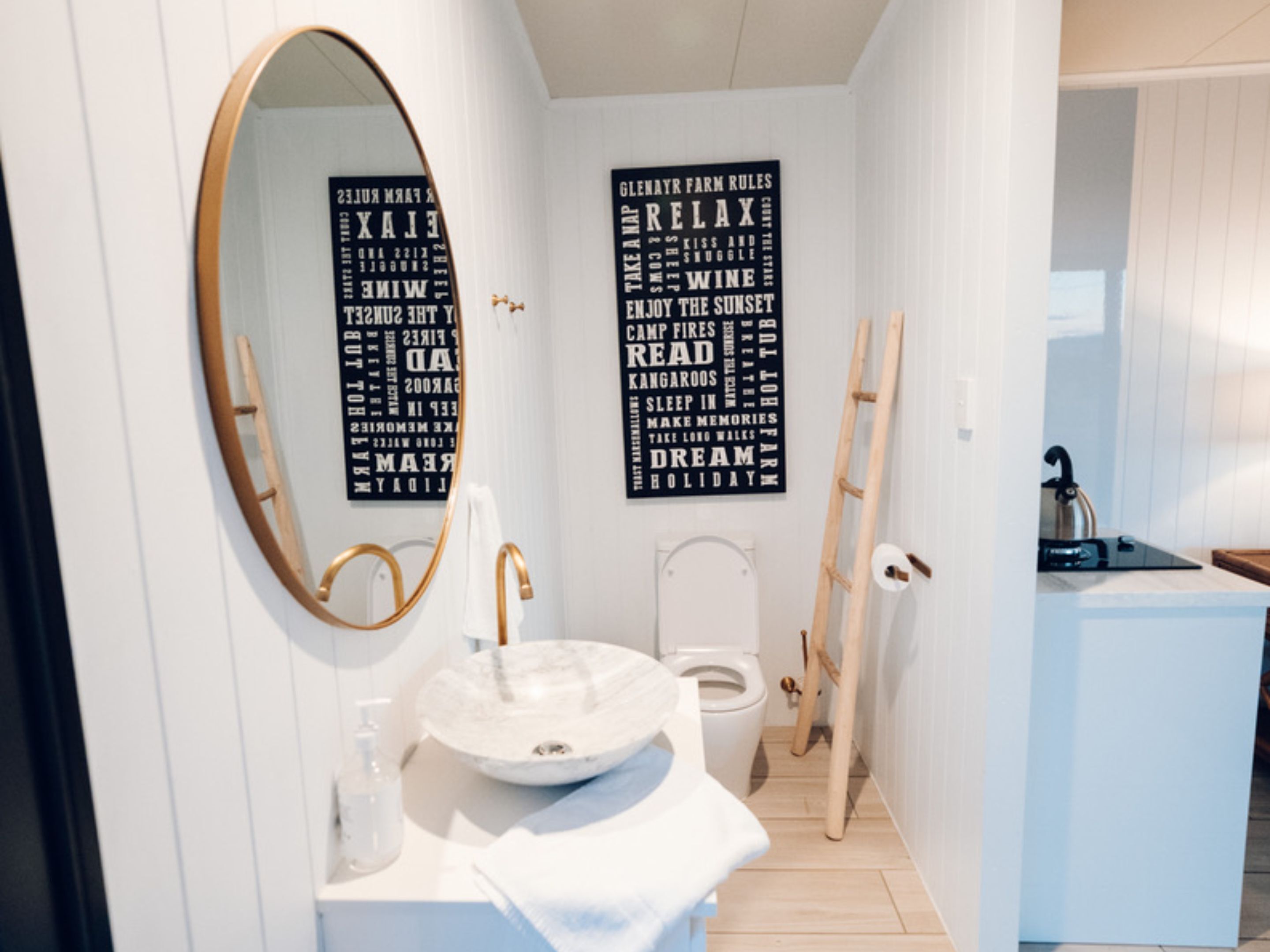 Un baño moderno con un espejo redondo, un lavamanos blanco y un inodoro. Hay dos piezas de arte mural negro con texto blanco.
