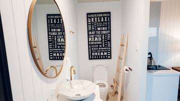Un baño moderno con un espejo redondo, un lavamanos blanco y un inodoro. Hay dos piezas de arte mural negro con texto blanco.