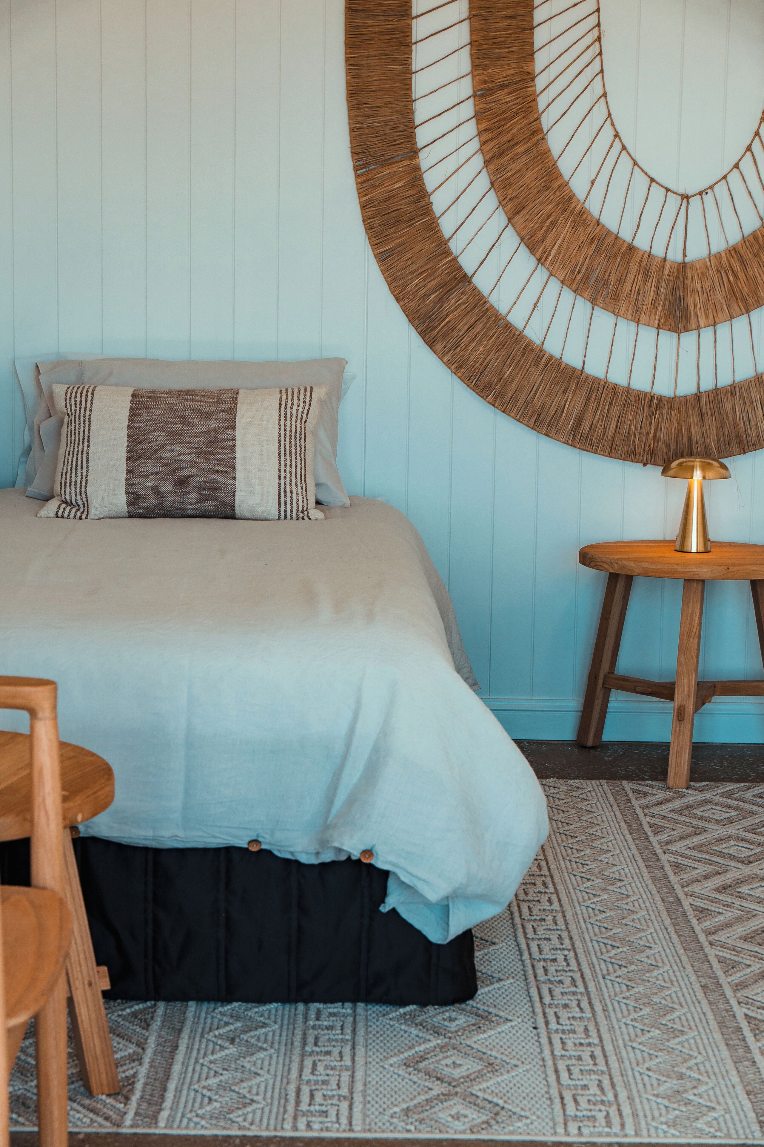 Een slaapkamer met een bed, een ronde wanddecoratie, een houten kruk en een kamerkleed met dessin.
