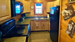 Una cocina compacta con armarios de madera, una estufa negra, un refrigerador y una ventana con vistas.