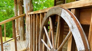 Una estructura rústica de madera con una rueda grande, barandillas de madera y una terraza de madera.