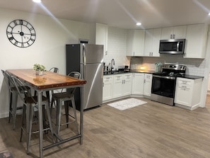 A modern kitchen with white cabinets, stainless steel appliances, a wooden dining table, and a wall clock.